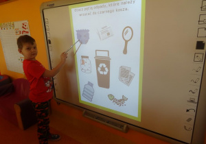 Chłopiec stoi pod tablicą interaktywną i wskaźnikiem pokazuje pampersa.